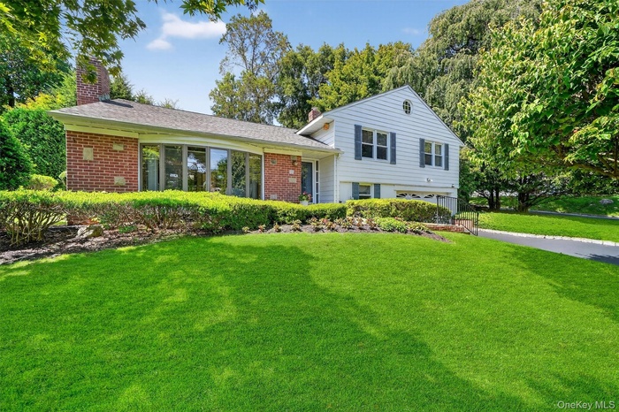 Split level home featuring a chimney, brick siding, and a front lawn