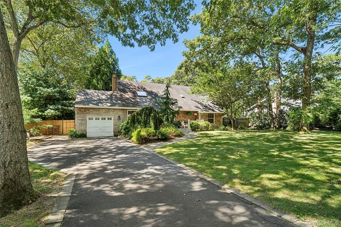 View of front facade with an attached garage, driveway, a chimney, and roof with shingles