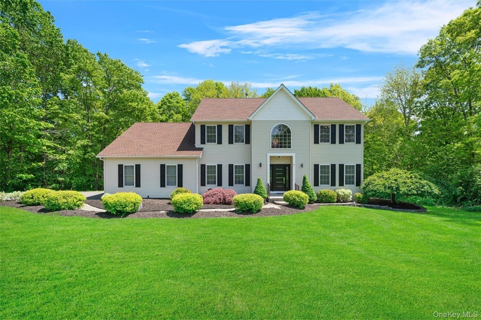 Colonial-style house featuring a front yard and roof with shingles