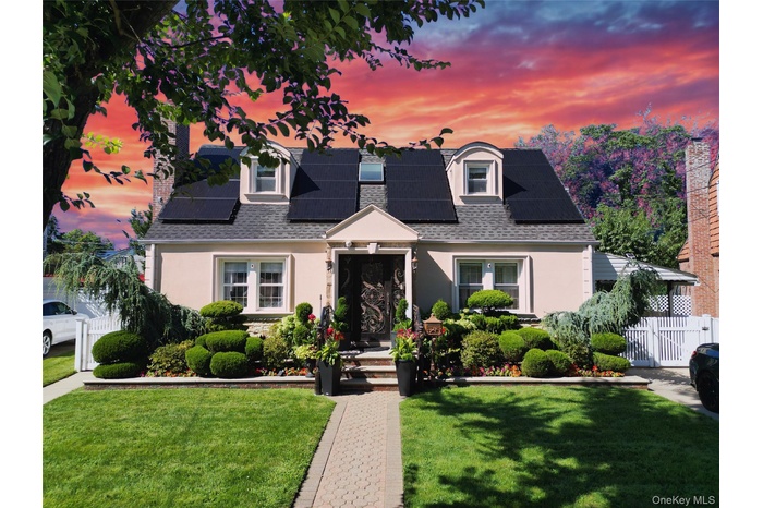 View of front of house featuring roof with shingles, stucco siding, solar panels, and a gate