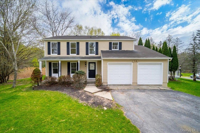 Traditional-style house with covered porch, an attached garage, a front yard, and aphalt driveway