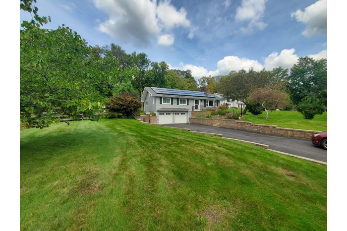 View of front facade featuring roof mounted solar panels, a front yard, driveway, an attached garage, and a chimney