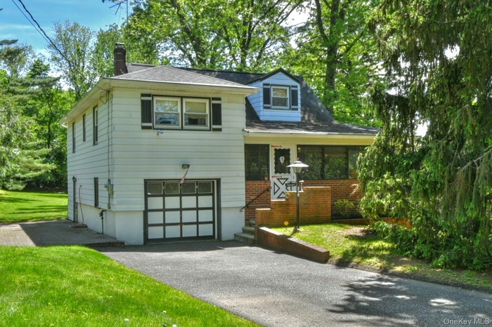 Split level home featuring a chimney, an attached garage, driveway, and a front lawn
