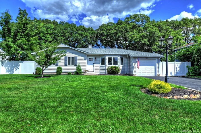 Ranch-style home featuring a garage, driveway, roof with shingles, and view of scattered trees