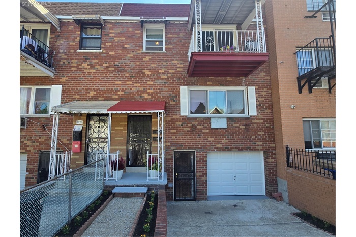View of front facade featuring an attached garage, a shingled roof, brick siding, concrete driveway, and a balcony