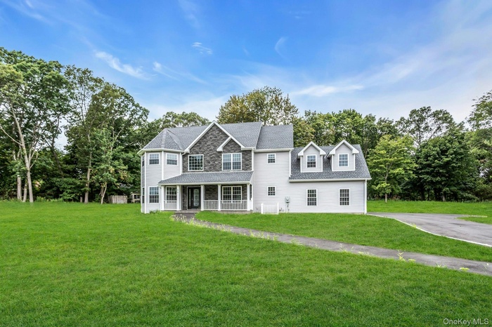 Back of property featuring a porch, a lawn, roof with shingles, and view of wooded area