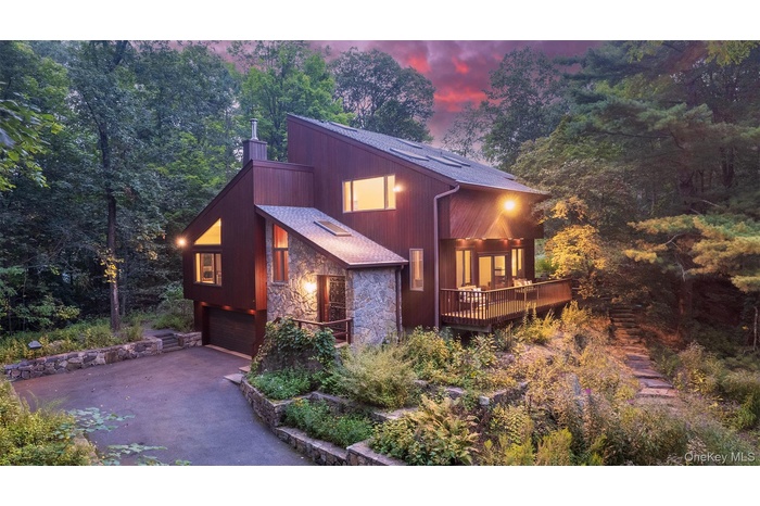 View of front of property featuring stone siding, driveway, a chimney, a garage, and a wooden deck