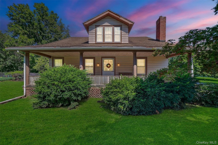 View of front of property with a lawn, a porch, a chimney, and a shingled roof