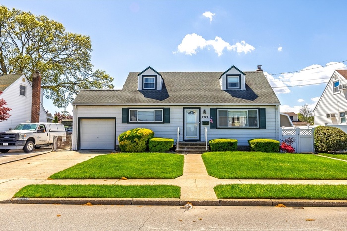Cape cod-style house featuring an attached garage, a shingled roof, and concrete driveway