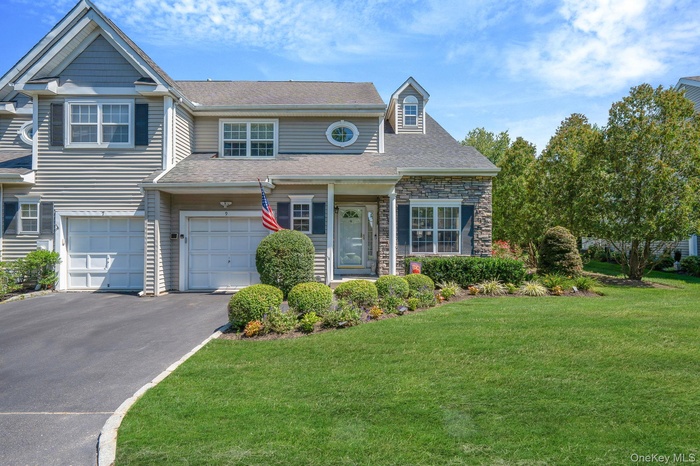 View of front of home with driveway, a front yard, an attached garage, stone siding, and roof with shingles