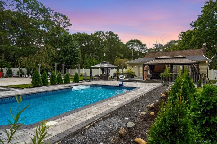 Pool at dusk featuring a gazebo, a patio, and view of scattered trees