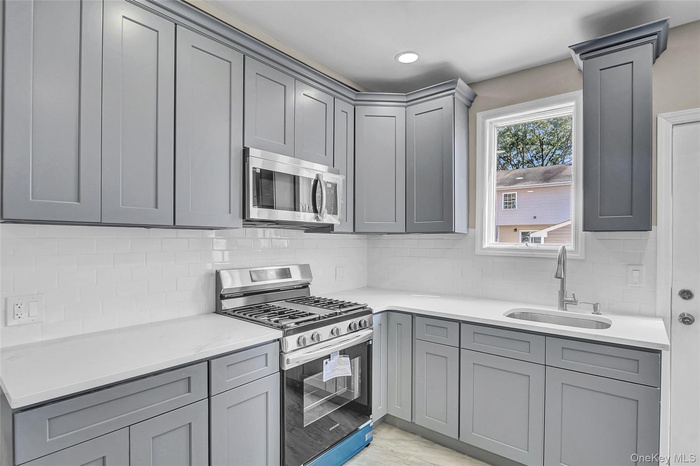 Kitchen featuring gray cabinetry, stainless steel appliances, backsplash, light stone countertops, and recessed lighting