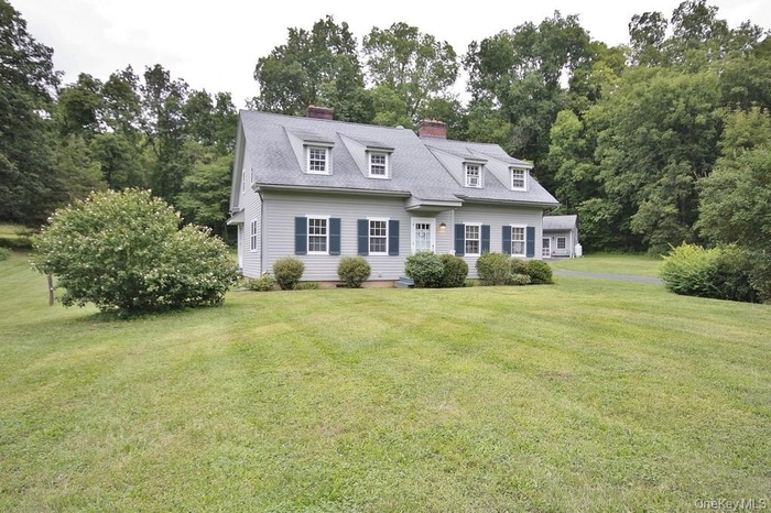Cape cod house featuring a front lawn, a chimney, and view of wooded area