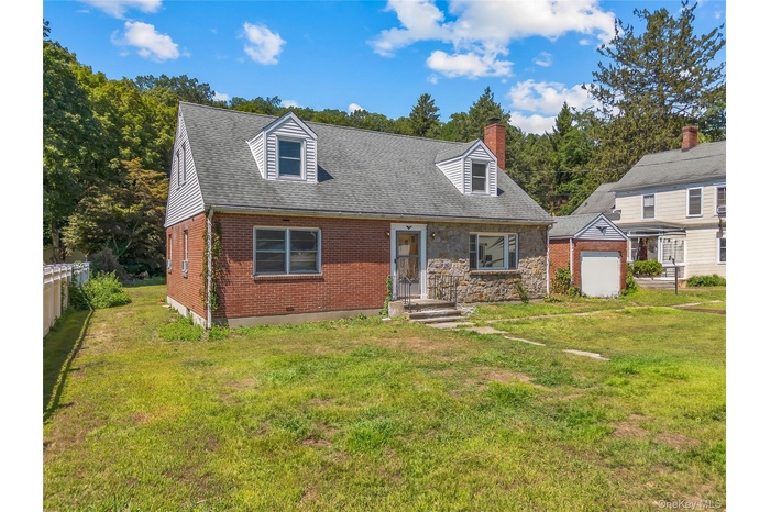 Cape cod home featuring a front yard, brick siding, roof with shingles, a chimney, and an outbuilding