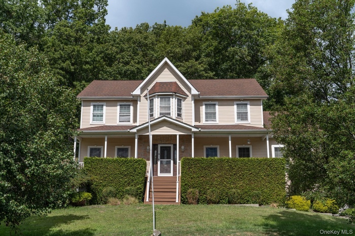 View of front facade with covered porch, a front lawn, and a shingled roof