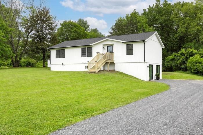 View of front of property with driveway, a front lawn, roof with shingles, and view of scattered trees