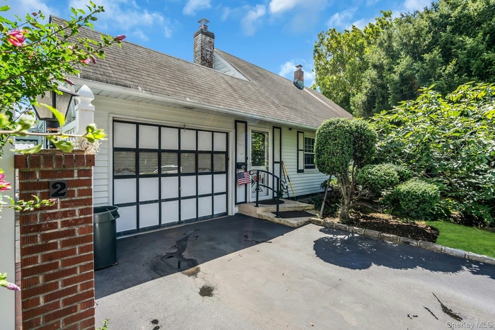 View of front facade with a shingled roof, asphalt driveway, a patio, and a chimney