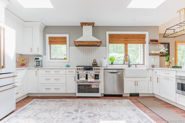 Kitchen featuring a skylight, white cabinets, backsplash, and appliances with stainless steel finishes