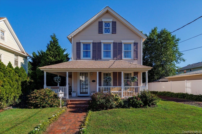 View of front of house with covered porch, a front yard, and roof with shingles