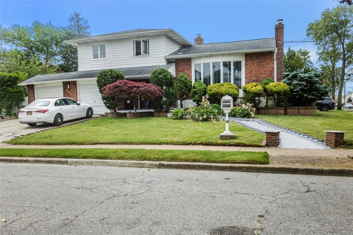 Tri-level home featuring a chimney, a front lawn, brick siding, and driveway