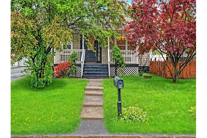 View of property hidden behind natural elements featuring a porch and a front lawn