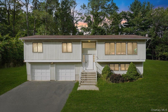 Raised ranch with a front lawn, driveway, a garage, and roof with shingles