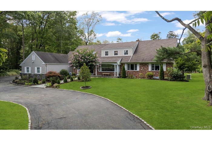 View of front of house featuring a front yard, driveway, brick siding, a chimney, and a shingled roof