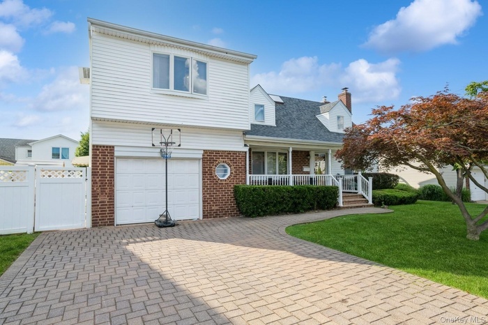 View of front facade with brick siding, covered porch, an attached garage, and decorative driveway