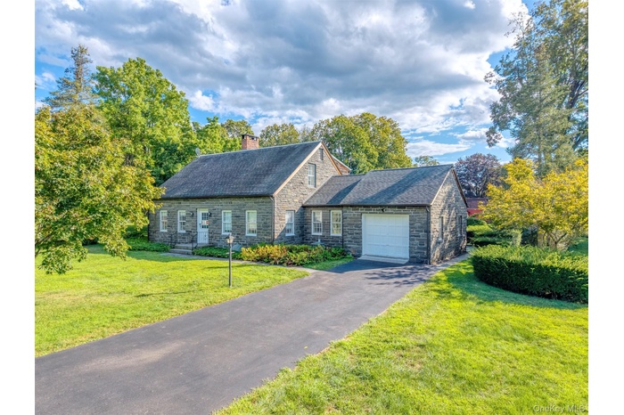 View of front of property featuring a garage, a front yard, stone siding, a chimney, and driveway