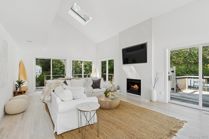 Living room with high vaulted ceiling, a skylight, wood finished floors, and a warm lit fireplace