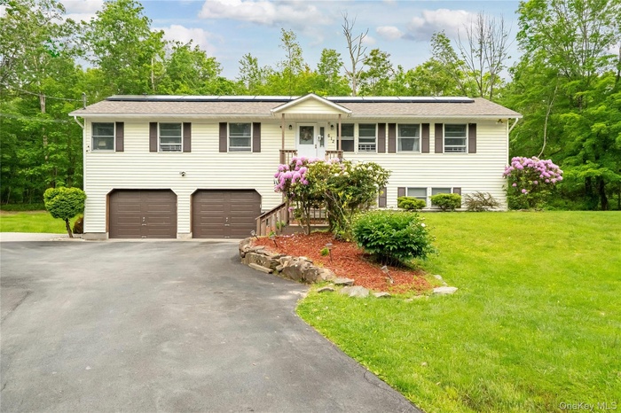 View of front of house featuring driveway, a front lawn, solar panels, and an attached garage