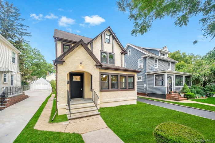 Tudor-style house featuring an outbuilding, a front yard, stucco siding, a garage, and a sunroom