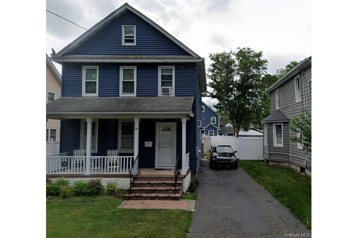Traditional style home with covered porch, a front yard, and asphalt driveway