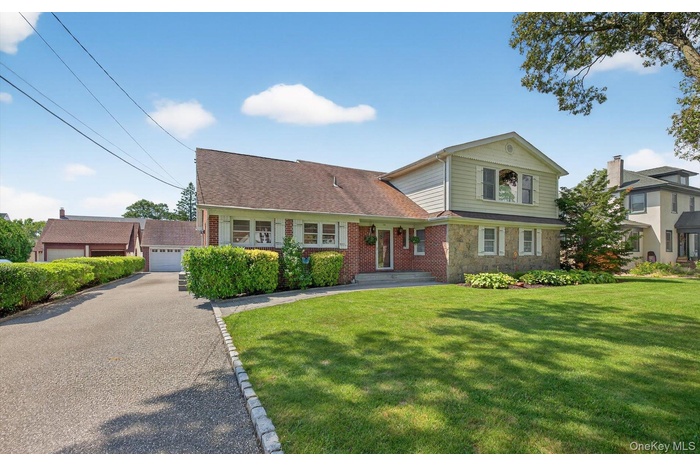 View of front of property featuring a front lawn, a shingled roof, stone siding, and a garage