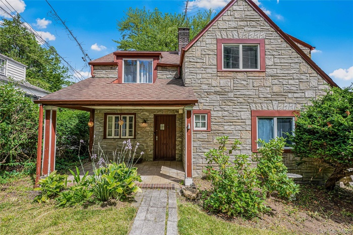 View of front of house featuring stone siding, roof with shingles, a chimney, and covered porch