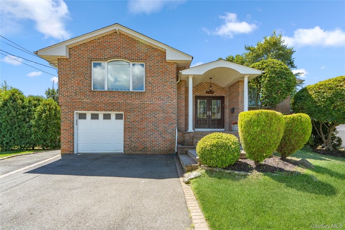 Raised ranch with driveway, brick siding, a garage, and french doors