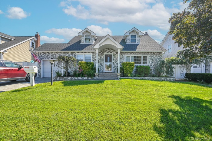 Cape cod-style house with stone siding, an attached garage, a shingled roof, and driveway