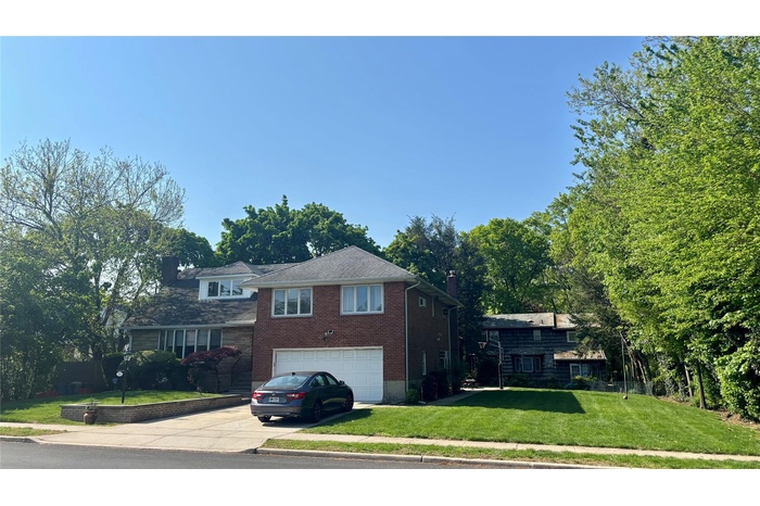 Tri-level home featuring concrete driveway, a garage, a chimney, a front lawn, and brick siding