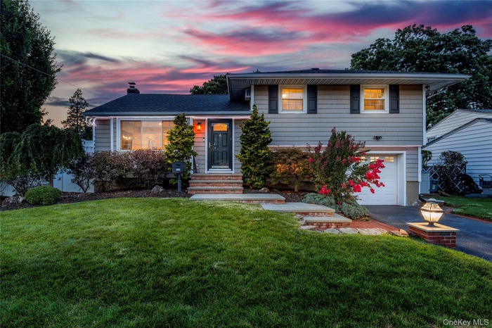 Split level home featuring a front lawn, an attached garage, asphalt driveway, and a chimney