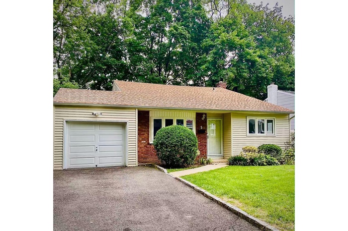 Ranch-style home featuring brick siding, a front lawn, asphalt driveway, a garage, and a chimney