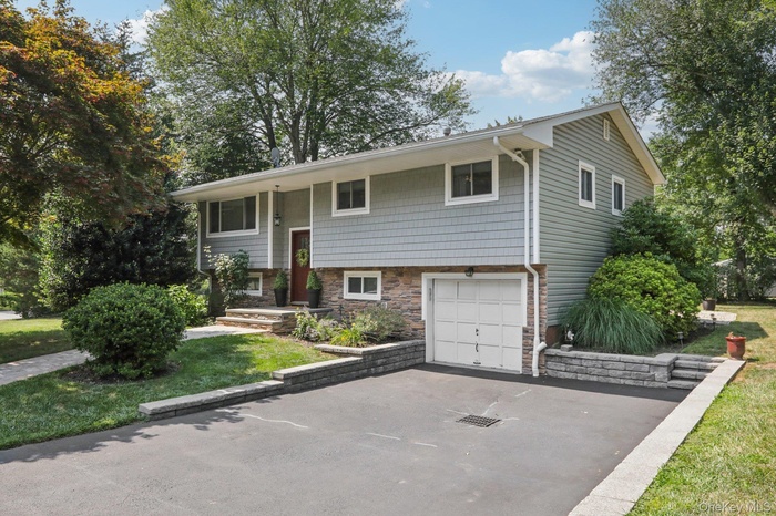 Split foyer home featuring stone siding, driveway, a garage, and a front yard