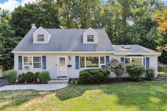 Cape cod-style house with a front yard, roof with shingles, a chimney, and view of scattered trees