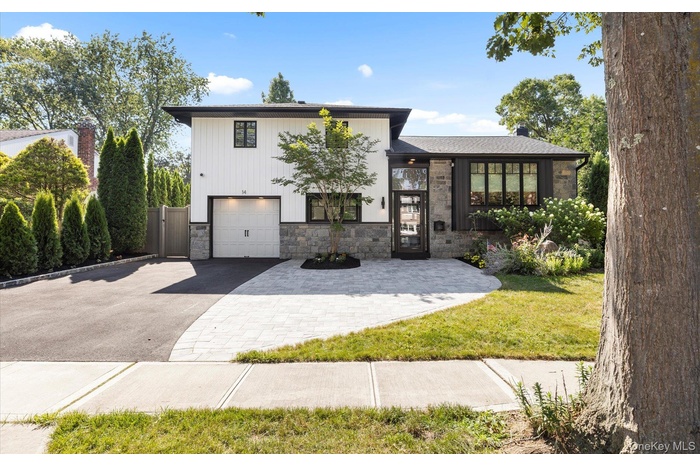 View of front of property featuring driveway, stone siding, a front lawn, and a garage