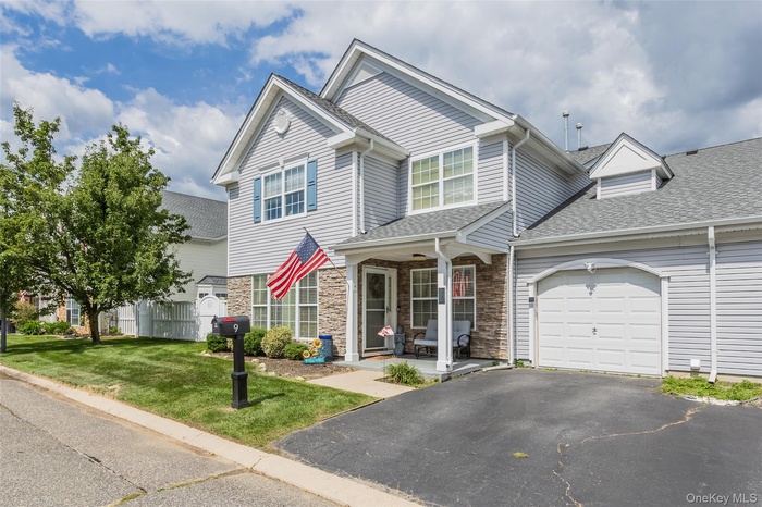 Traditional home featuring a porch, asphalt driveway, a garage, stone siding, and a shingled roof