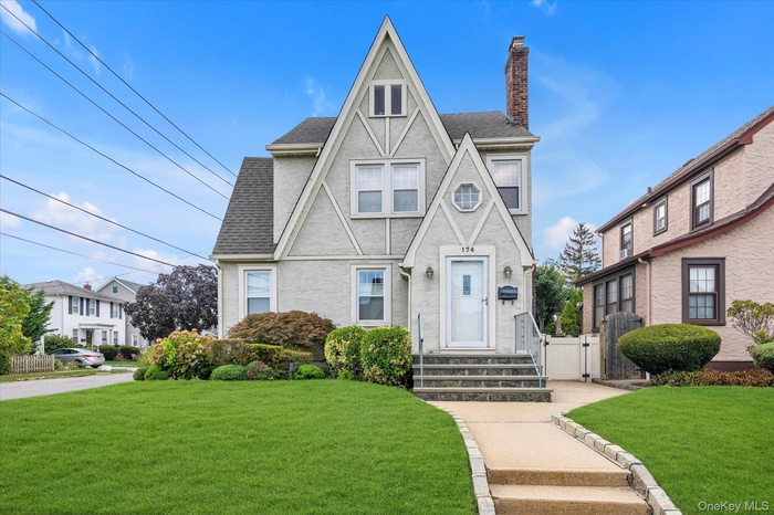 English style home featuring a gate, stucco siding, a chimney, and a shingled roof