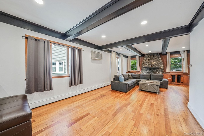 Living room featuring beamed ceiling, light wood-type flooring, a baseboard heating unit, a fireplace, and recessed lighting