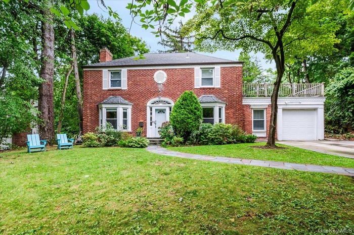 Colonial house with a garage, a chimney, brick siding, a front yard, and concrete driveway
