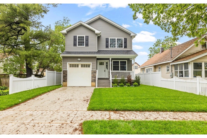 View of front facade featuring covered porch, an attached garage, driveway, and stone siding
