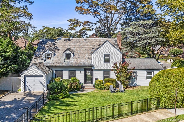 Cape cod house featuring concrete driveway, a fenced front yard, a garage, a high end roof, and a chimney