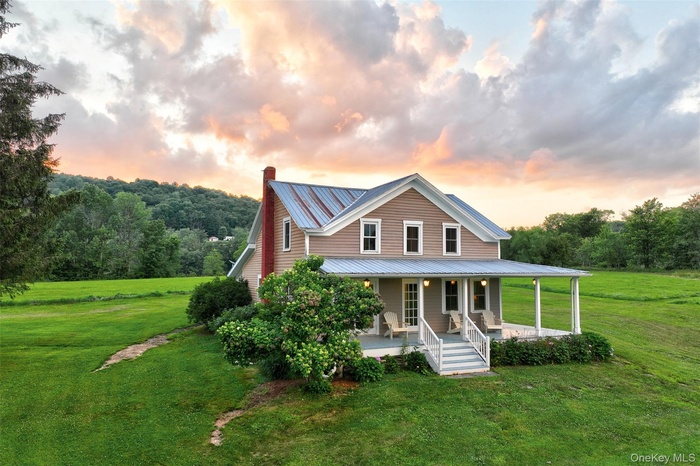 View of front of home with a lawn, covered porch, a metal roof, and a chimney